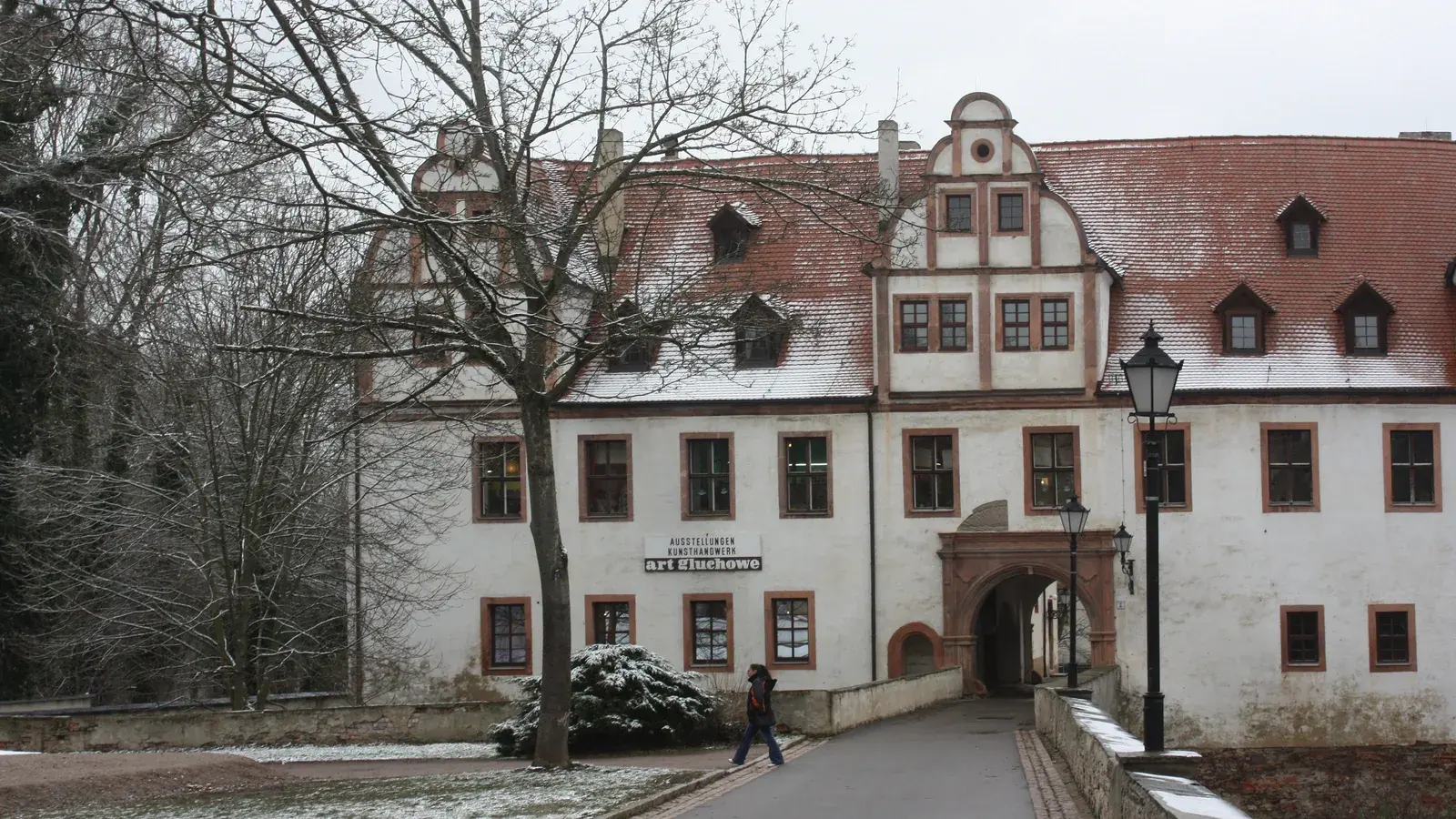 Archivaufnahme vom 16. Februar 2016: Die helle Fassade von Schloss Forderglauchau mit roten Fensterrahmen und verschneitem Ziegeldach steht hinter kahlen Bäumen; eine Person geht über den Weg vor dem Gebäude. Das Bild zeigt nicht die Nacht der Schlösser 2026.