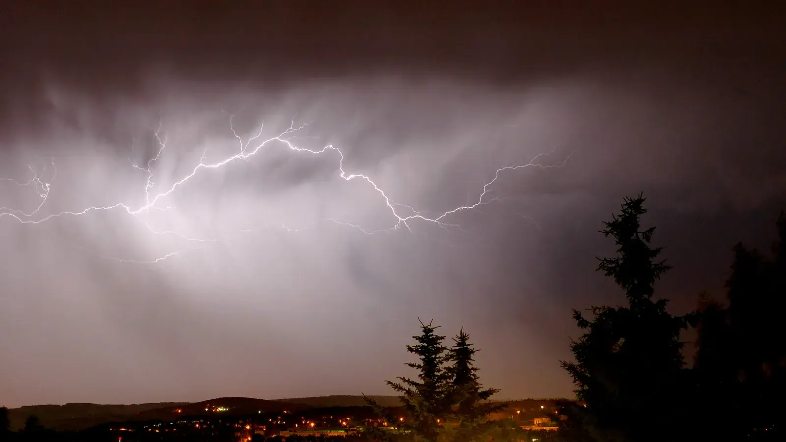 Archivaufnahme von 2005: Verzweigte Blitze leuchten in einer Gewitterwolke über nächtlichen Häusern und dunklen Nadelbäumen in Zwickau.