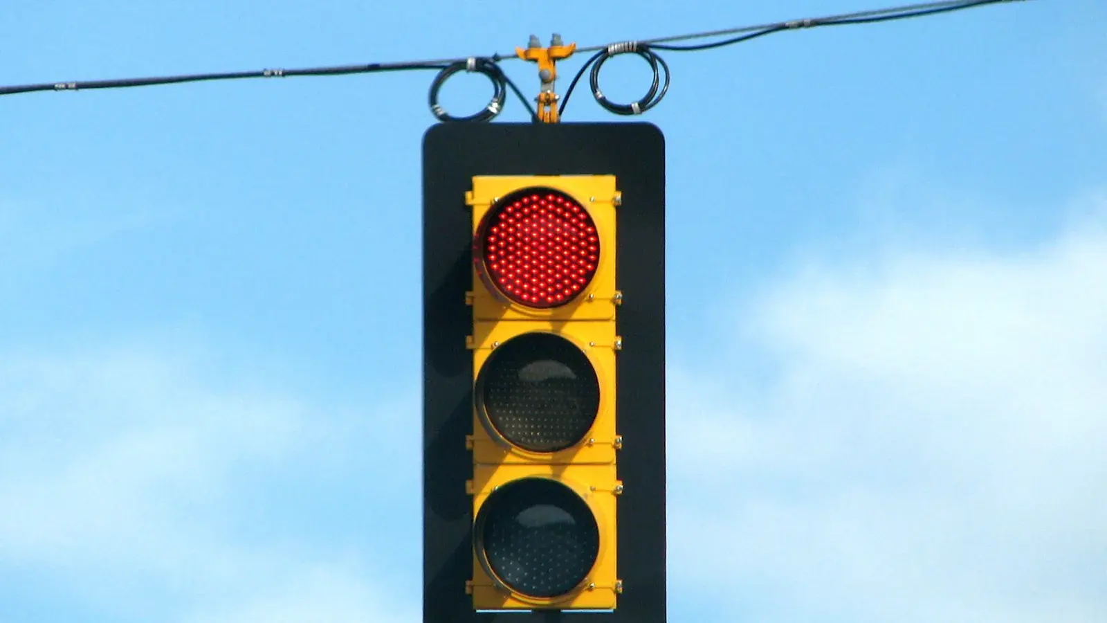 Symbolbild: An einer gelben Ampel vor blauem Himmel leuchtet das obere rote LED-Signal.
