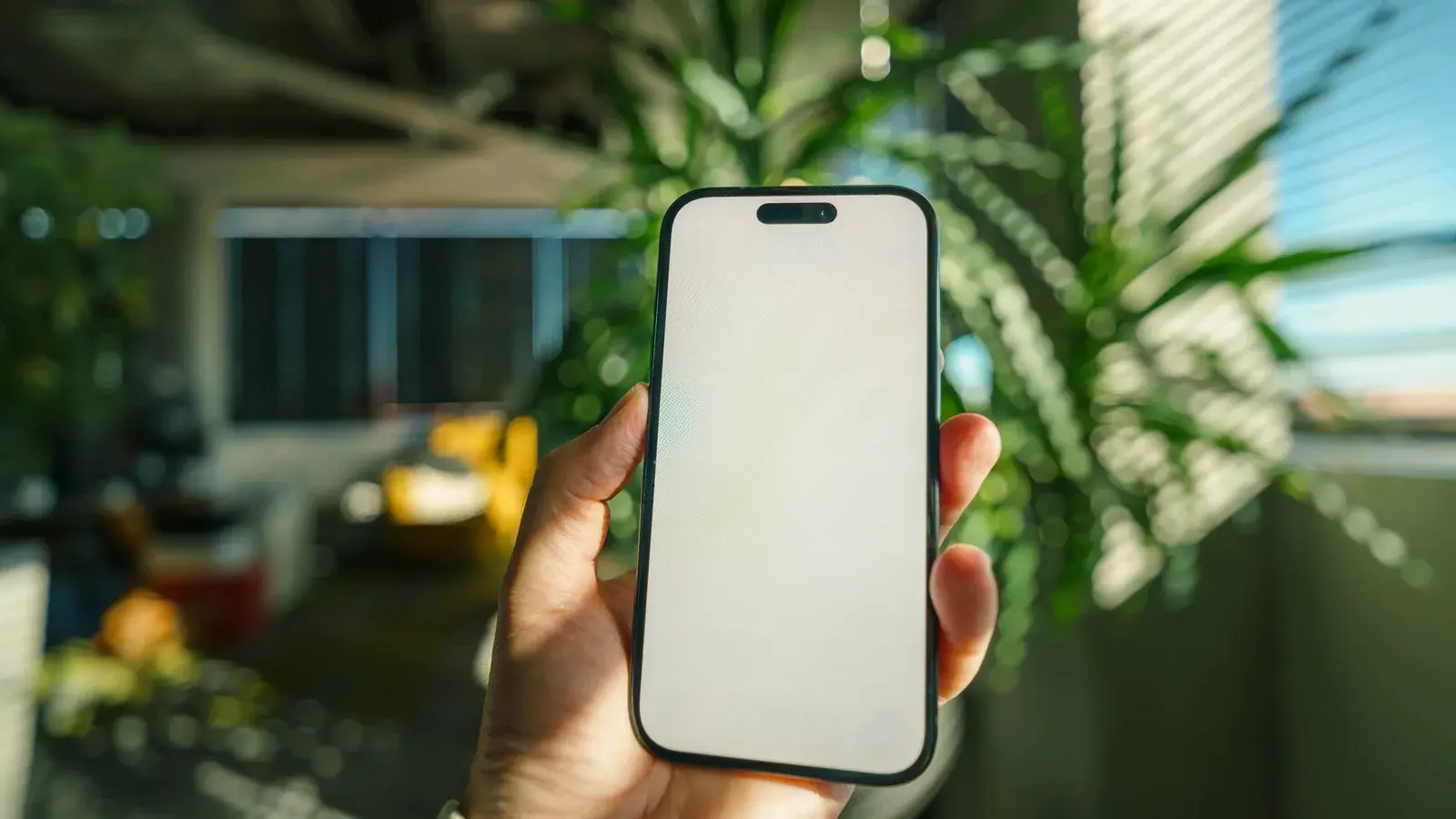 Symbolbild: Eine Hand hält in einem hellen Raum ein Smartphone mit vollständig weißer, leerer Anzeige.