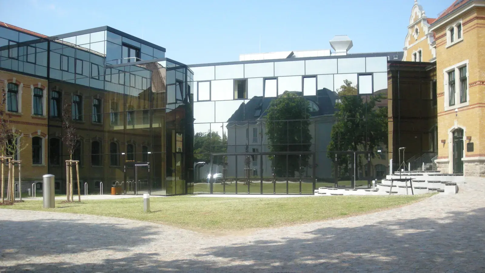 Archivaufnahme vom 10. Juli 2013: Im Innenhof des Robert-Schumann-Konservatoriums in Zwickau verbindet ein moderner verglaster Bau zwei gelbe Backsteingebäude; davor liegen Rasen, Pflaster und eine breite Freitreppe. Das Bild zeigt nicht den Sommerempfang 2026.