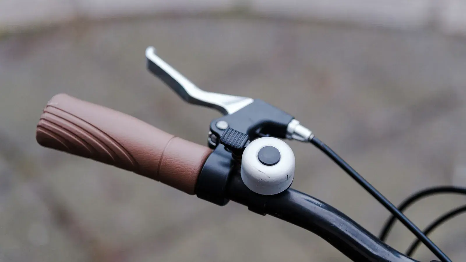 Nahaufnahme eines braunen Fahrradgriffs mit Bremshebel und silberner Klingel