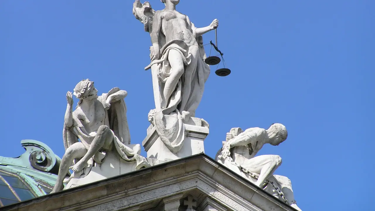 Justitia mit Waage als Figurengruppe auf dem Justizpalast in München vor blauem Himmel