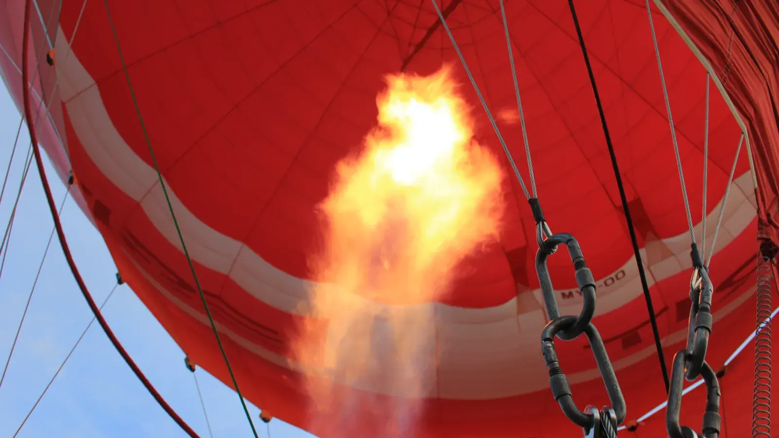 Symbolbild von 2012: Eine helle Flamme schießt aus dem Brenner in die rot-weiße Hülle eines Heißluftballons; Seile und Metallstreben rahmen den Brenner ein.