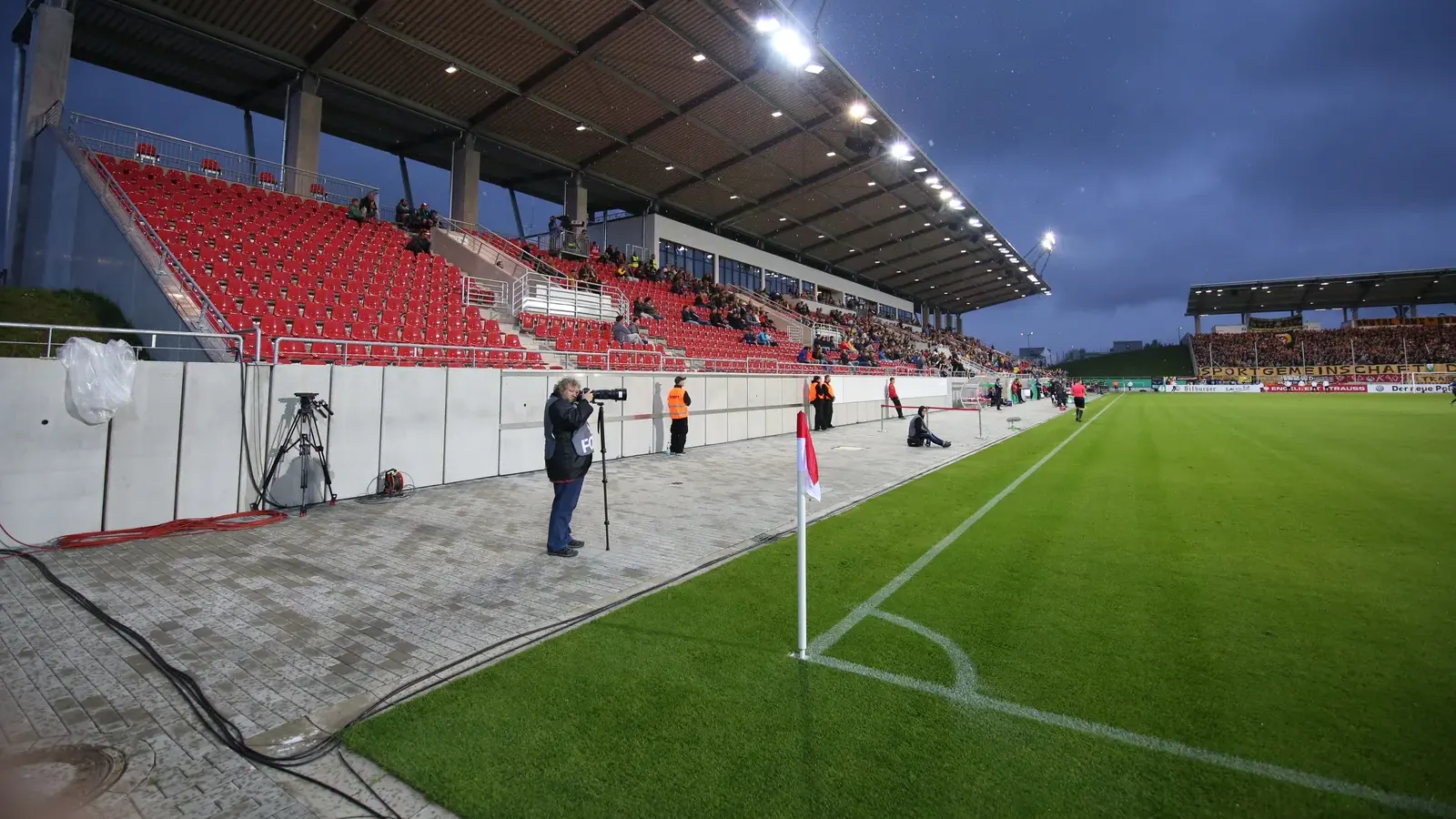 Archivaufnahme von 2017: Eine überdachte Tribüne mit roten Sitzen steht an der Ecke des grünen Spielfelds im Stadion Zwickau unter eingeschaltetem Flutlicht.