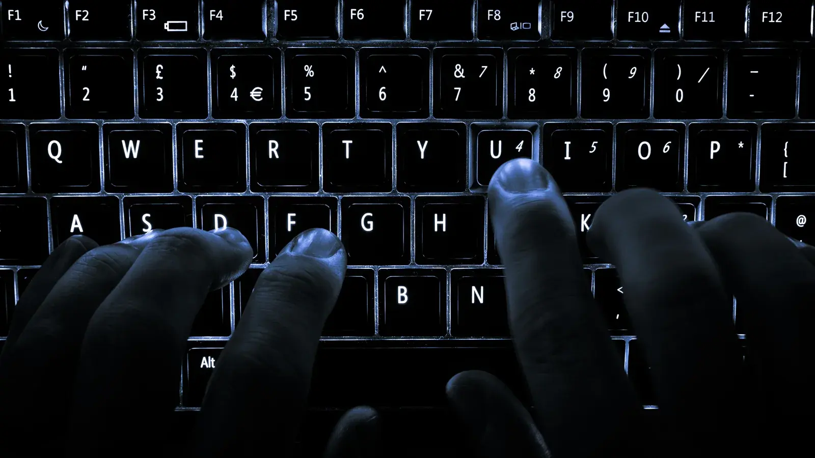 Symbolbild: Zwei Hände tippen auf einer blau beleuchteten schwarzen Computertastatur.