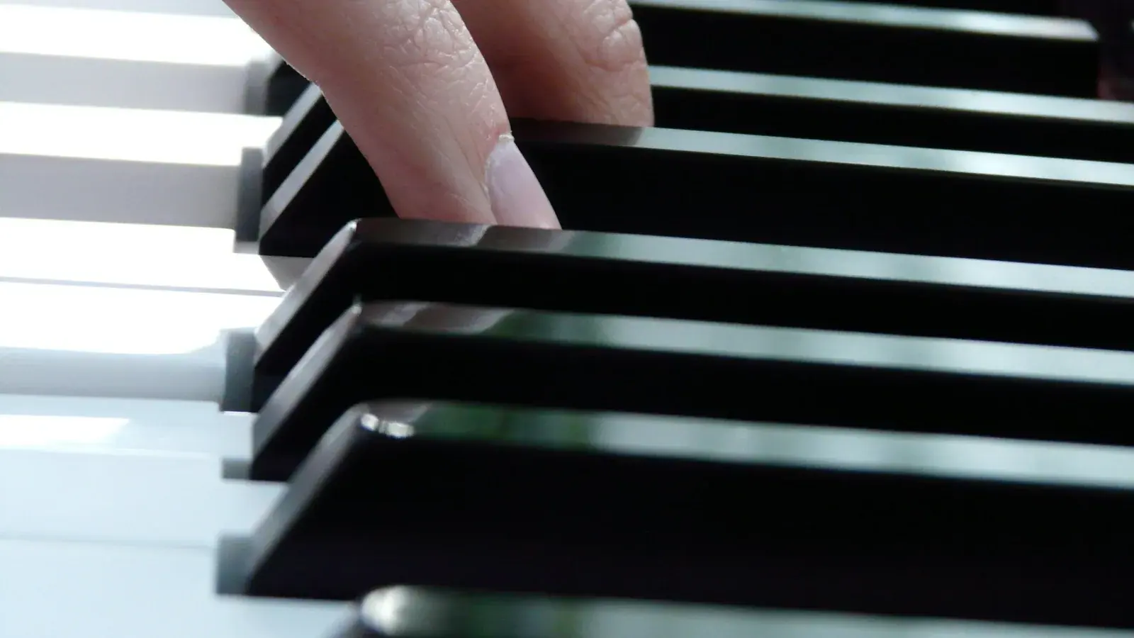 Symbolbild: Die Finger einer Hand liegen in Nahaufnahme auf schwarzen und weißen Klaviertasten.