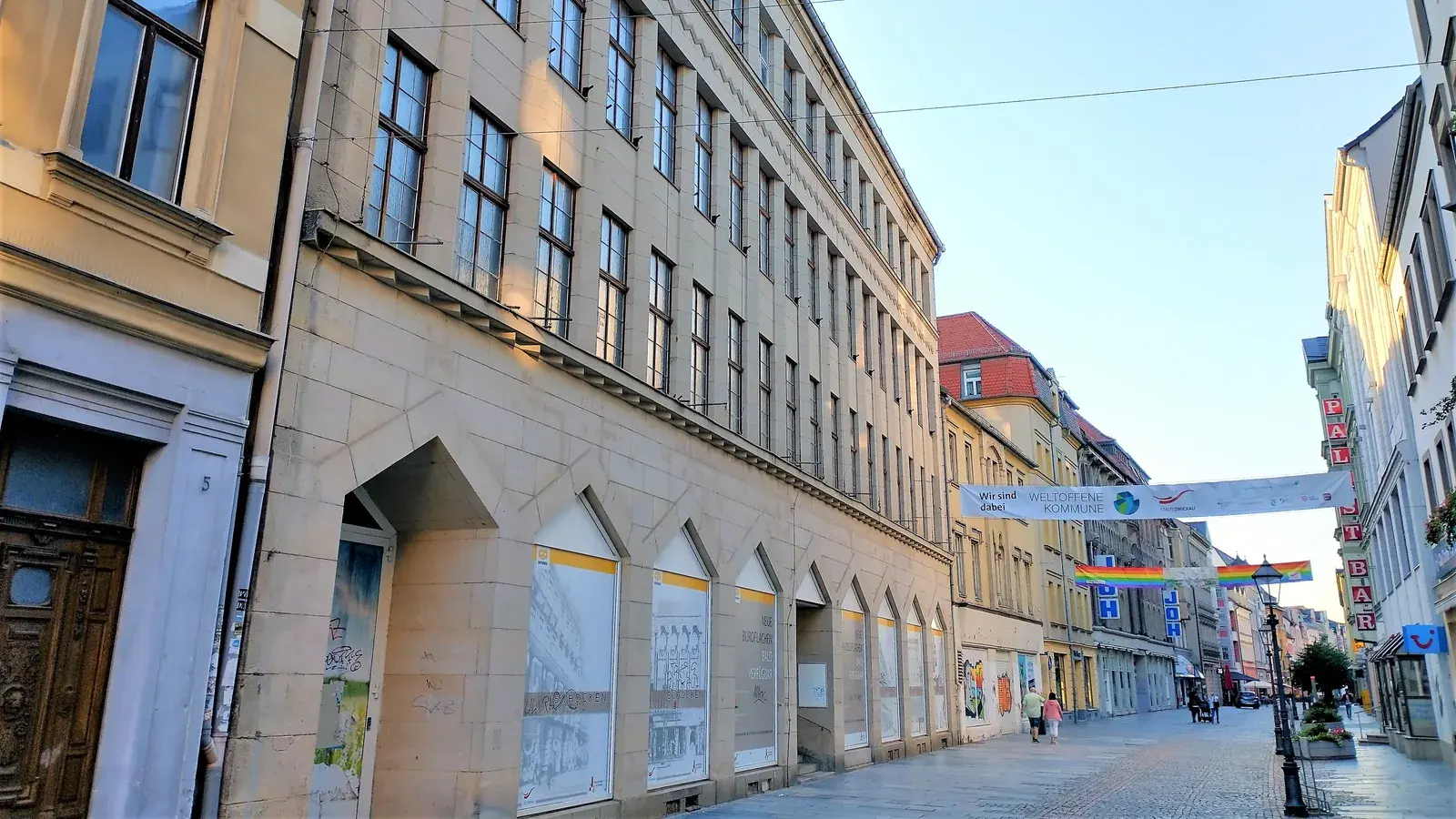 Archivaufnahme von 2021: Blick entlang der hellen, mehrgeschossigen Fassade des ehemaligen Kaufhauses Schocken in Zwickau; in den zugedeckten Erdgeschossfenstern steht mehrfach „SCHOCKEN“.
