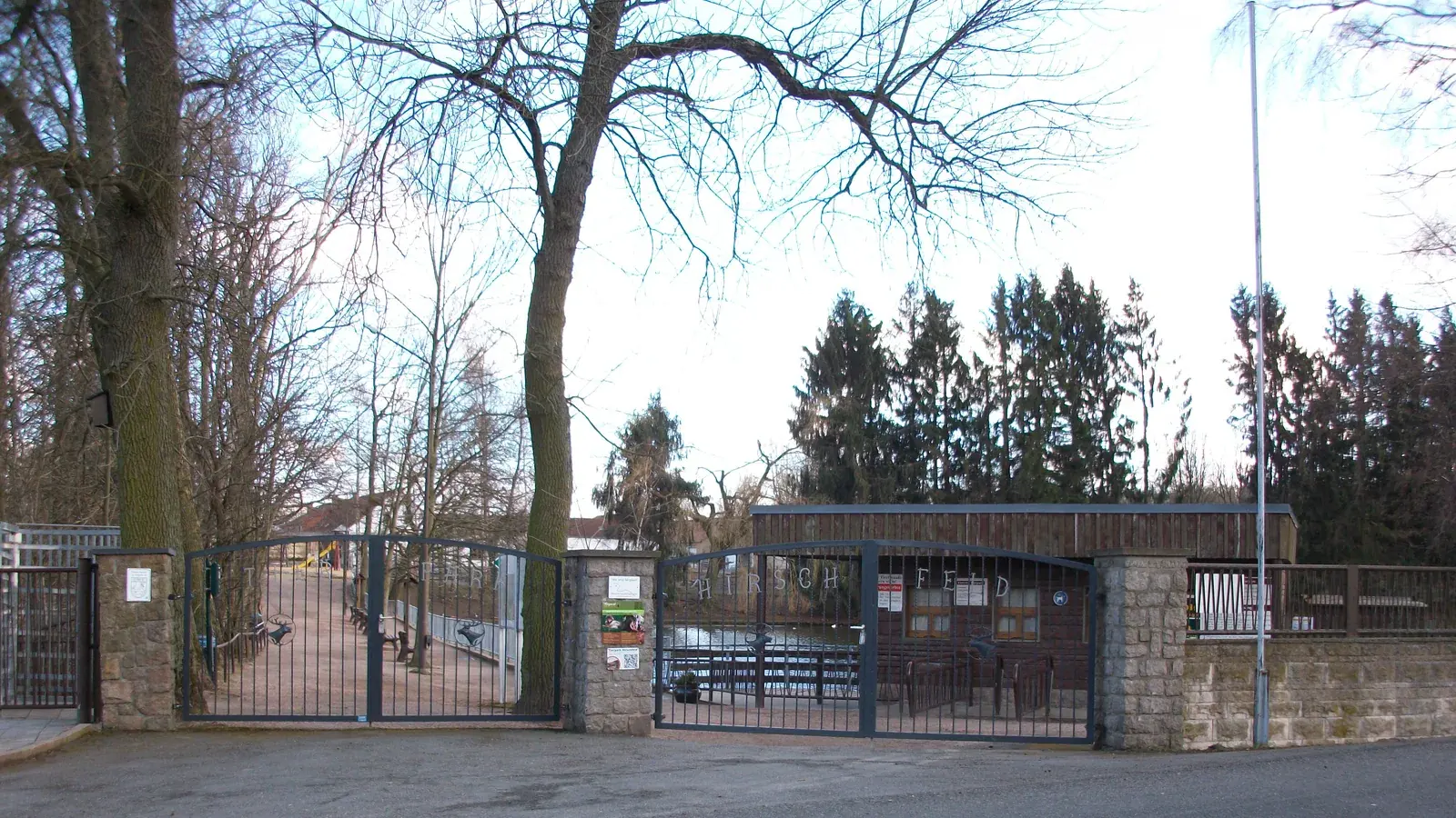 Eingangstor des Tierparks Hirschfeld mit Steinpfeilern, Kassenhäuschen und hohen Bäumen