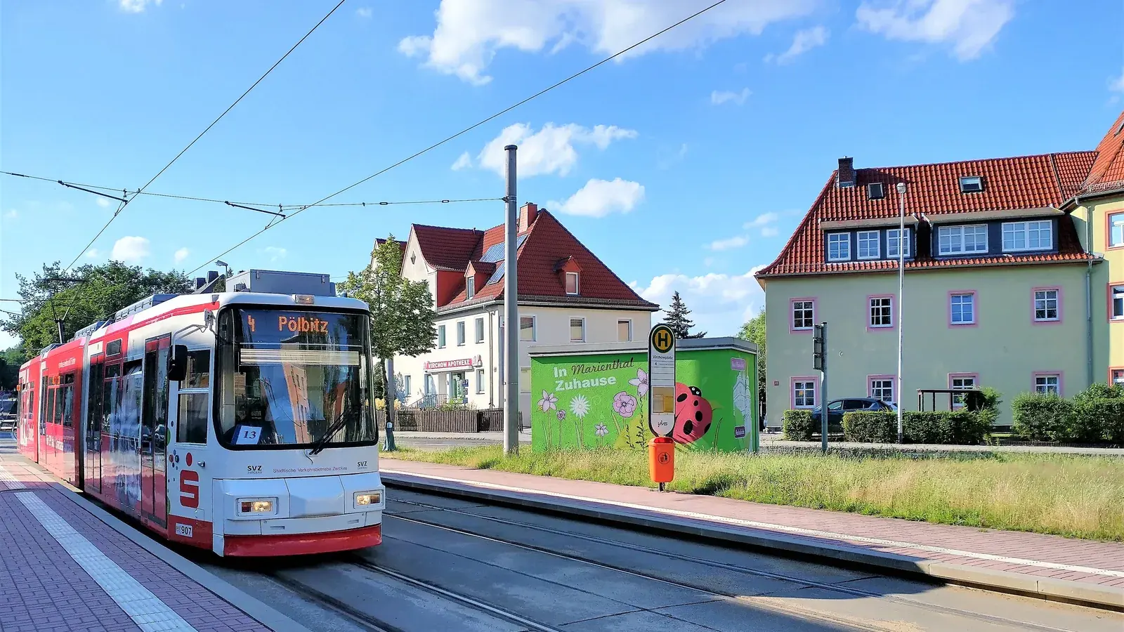 Rot-weiße Zwickauer Straßenbahn an einer Haltestelle in Marienthal vor Wohnhäusern.