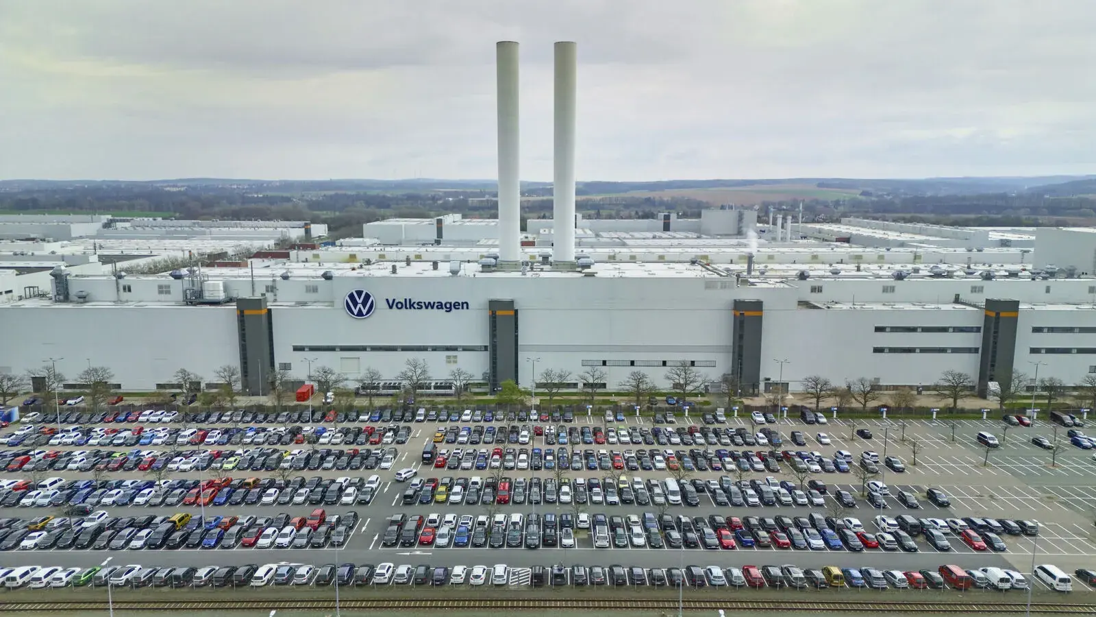Archivaufnahme aus dem Volkswagen Newsroom vom Mai 2026: Die helle Fassade des Zwickauer Volkswagenwerks mit großem VW-Zeichen und Volkswagen-Schriftzug steht hinter einem weitläufigen Parkplatz voller Fahrzeuge.