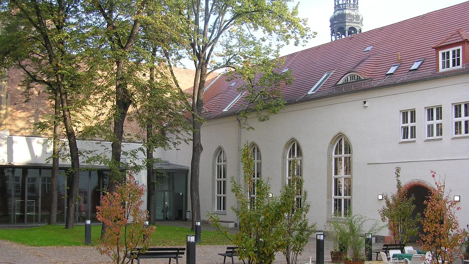 Archivaufnahme von 2006: Im Grünhainer Klosterhof am Zwickauer WHZ-Innenstadtcampus stehen Bäume und Bänke vor der hellen Aula mit Spitzbogenfenstern und rotem Dach.